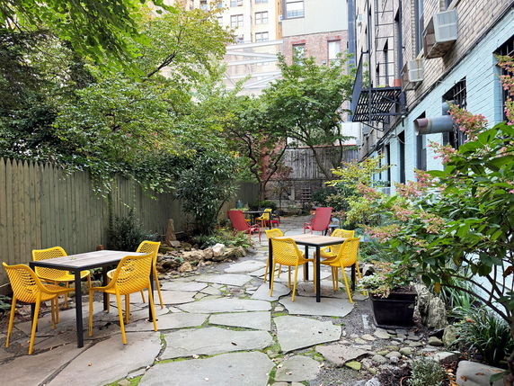 Outdoor seating area with yellow chairs and tables surrounded by trees and plants.