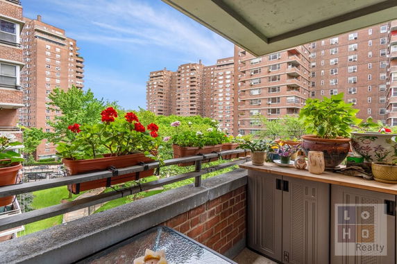 Balcony view showing nearby residential buildings and garden area with potted plants.