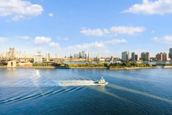 Panoramic view of a cityscape with a bridge, skyscrapers, and a river with a boat.