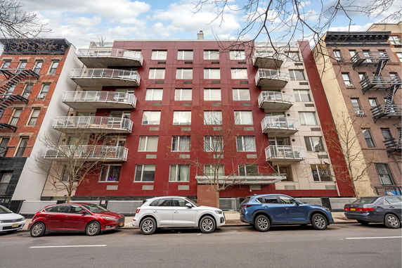 Front view of a multi-story residential building with balconies and parked cars.