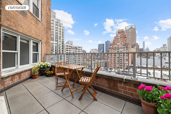 Rooftop terrace with a small table and chairs, offering a view of surrounding high-rise buildings.