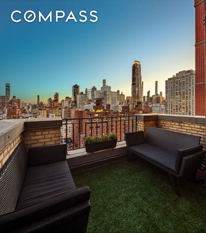 Rooftop seating area with wicker sofas overlooking city skyline at dusk.