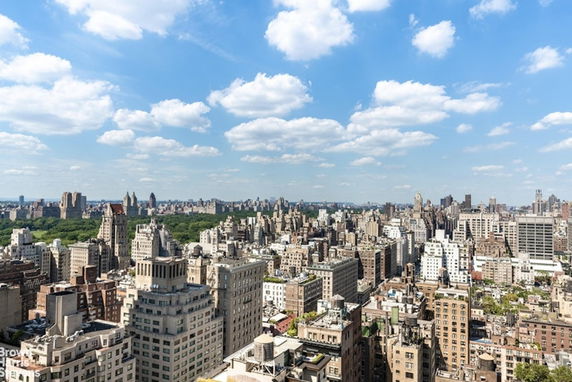 Panoramic view of a city skyline with numerous tall buildings under a partly cloudy sky.