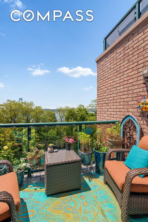 Outdoor patio area with seating and potted plants, overlooking a scenic view of trees and a distant body of water.