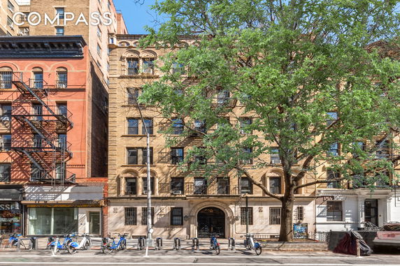 Front view of a multi-story brick building with fire escapes and an arched entrance.