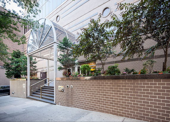 Front view of a building entrance with a glass canopy and brick wall.