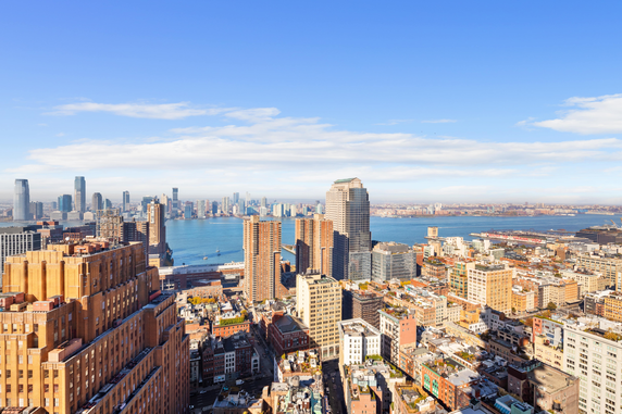 Panoramic view of a city skyline with numerous tall buildings and a body of water in the background.