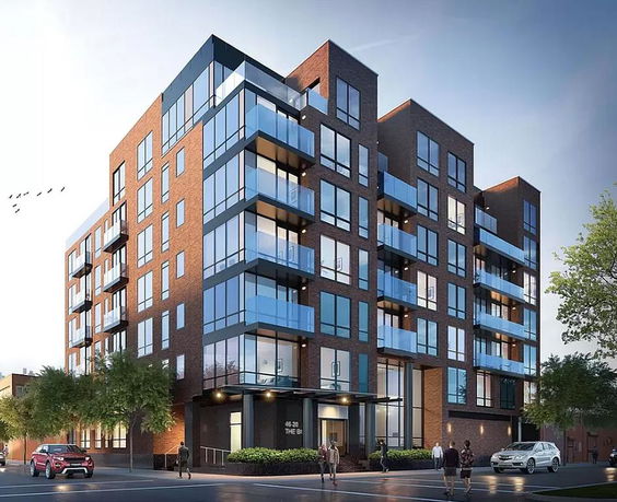 Front view of a modern multi-story apartment building with glass balconies and brick facade.