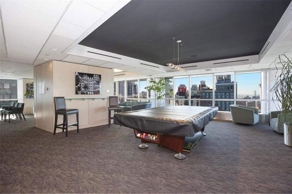 Interior view of a recreation area with a covered pool table and seating, featuring large windows with city views.