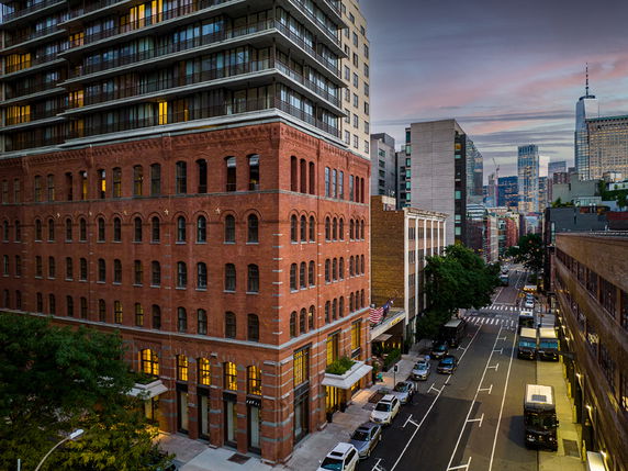 View of a city street with a prominent brick building and high-rise structures in the background.