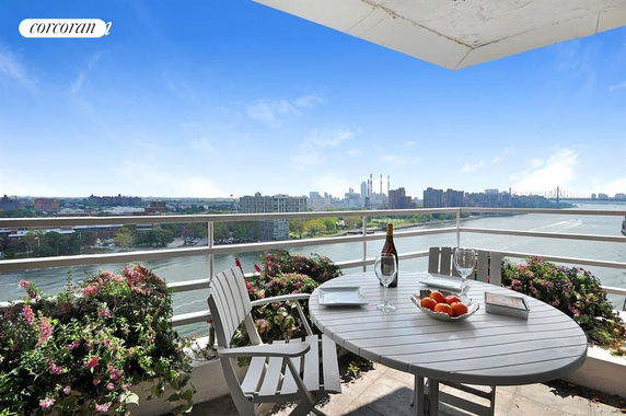 Panoramic view from a balcony overlooking a river, with table and chairs in the foreground.