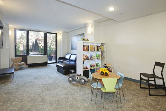 Indoor play area with children's furniture, a bookshelf with toys and books, and a seating area with a sofa.