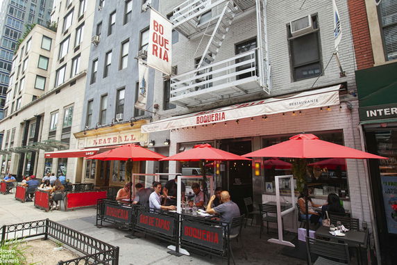 Front view of a multi-story building with outdoor seating under red umbrellas.