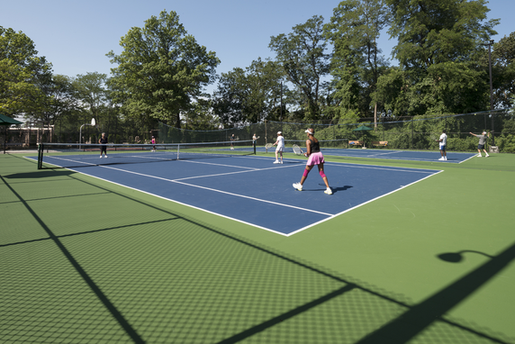 Tennis courts with players and surrounding trees.