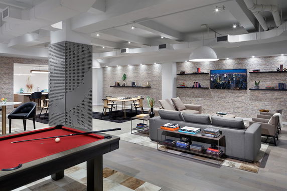 Interior view of a modern recreational area with seating, a pool table, and shelves with books.