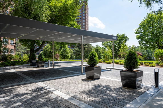 Covered parking area with large potted plants and brick paving.