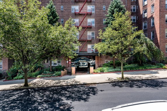 Front view of a multi-story brick apartment building with a main entrance canopy and surrounding trees.