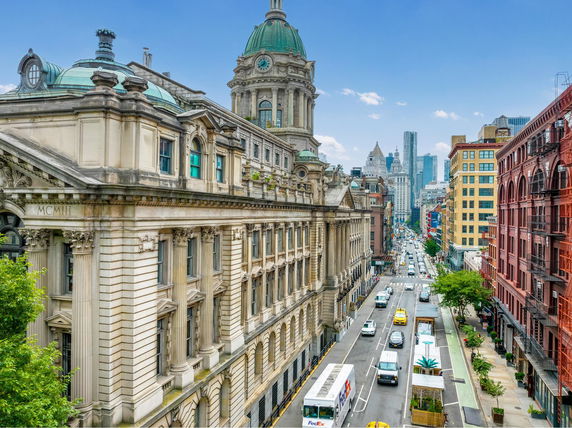 Street view of a historic building with detailed facade and dome, alongside traffic-filled road in a city.