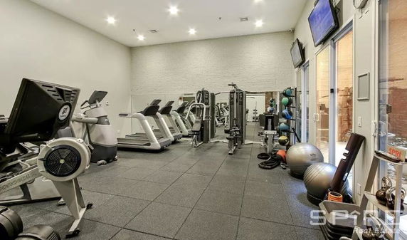 Indoor gym area with various exercise equipment and wall-mounted TVs.