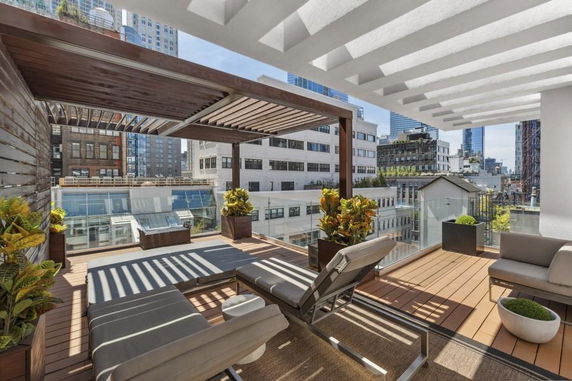 Rooftop with seating area and pergola overlooking city buildings.