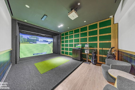 Indoor golf simulation room with golf equipment and seating.