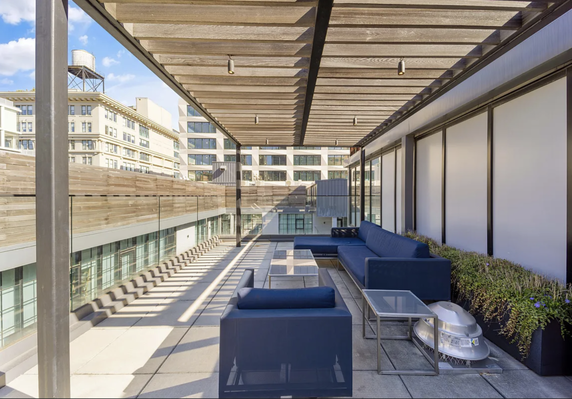 Rooftop area with seating and a pergola, featuring modern furniture and glass railings.