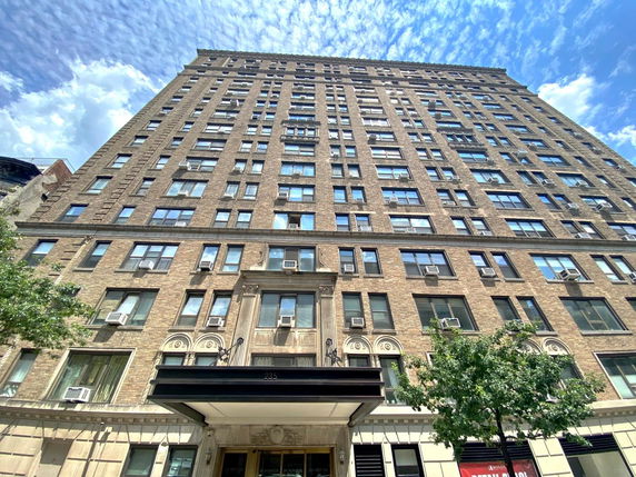 Front view of a multi-story brick apartment building with numerous windows and air conditioning units.