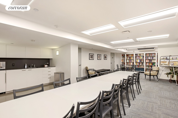 Interior view of a community room with tables, chairs, bookshelves, and a kitchenette.