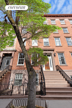 Front view of a multi-story brick townhouse with stairs leading to the main entrance.