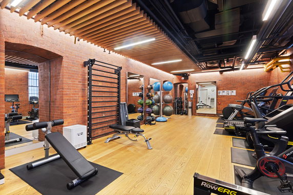 Interior view of a fitness gym with brick walls, exercise equipment, and wooden flooring.