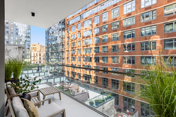 View from a building balcony overlooking surrounding apartment buildings with glass railings and outdoor seating.