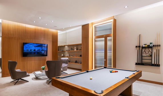 Interior of a recreational room with a pool table, modern chairs, and a wall-mounted TV.