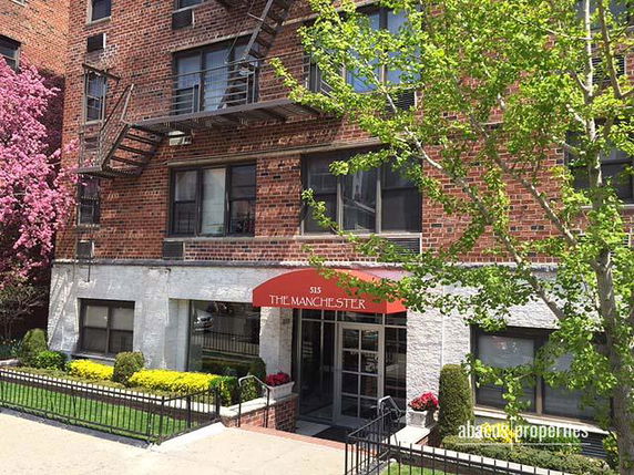 Front view of a brick apartment building with a red awning and fire escape.