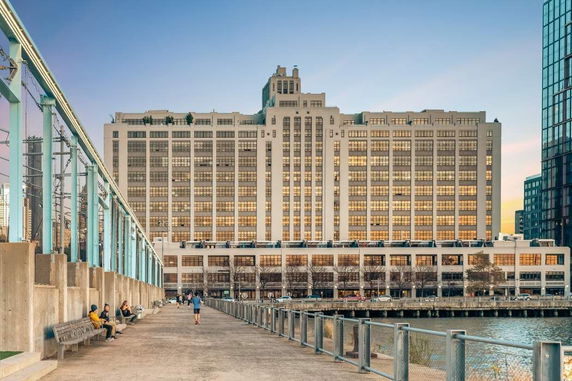 Front view of a large multi-story building with numerous windows, situated near a waterfront.