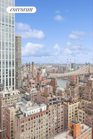 View of multiple apartment buildings and a bridge with a river and cityscape in the background.