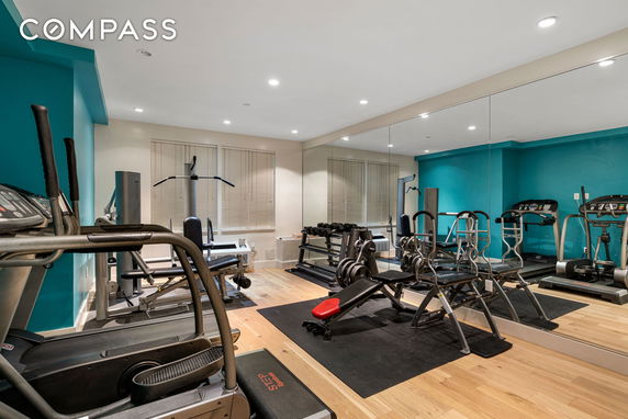 Room equipped with exercise machines and weightlifting equipment, featuring large mirrors and teal walls.