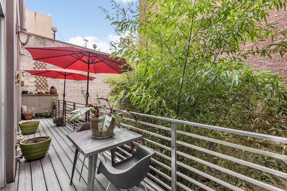 Outdoor balcony area with table and chairs, red umbrellas, and potted plants.