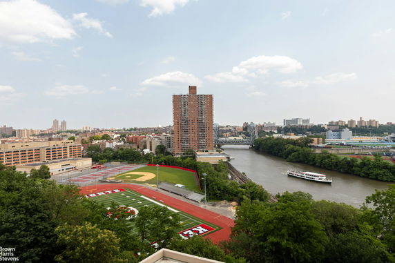 Panoramic view of a cityscape with a river, tall building, sports field, and bridge.