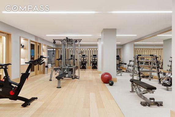 Interior view of a gym with exercise equipment, including bikes, weights, and benches.