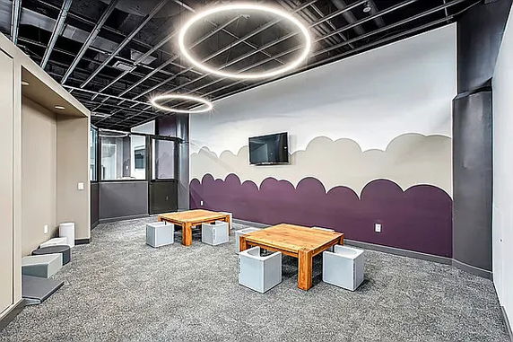 Indoor play area with low wooden tables, cube seats, and circular ceiling lights.