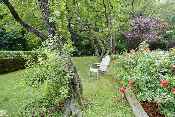 Outdoor view of a garden with trees, flowers, and a wooden chair.