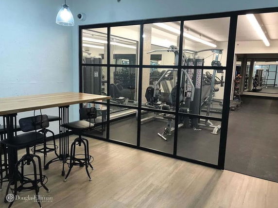 Interior view of a gym area with exercise equipment and adjacent table with stools.