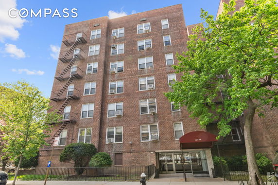 Front view of a multi-story brick apartment building with fire escapes and an entrance awning.