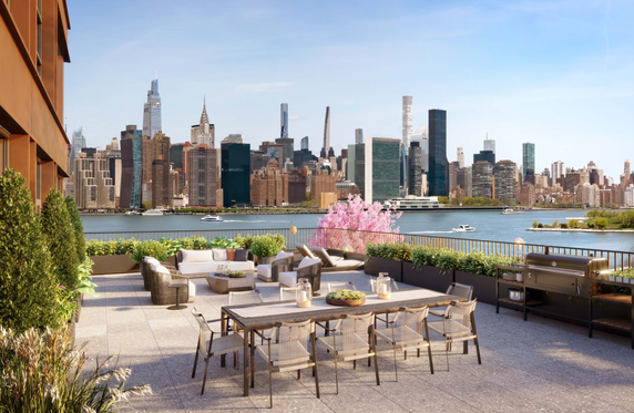 Rooftop terrace with outdoor furniture, dining area, and views of a city skyline across a river.