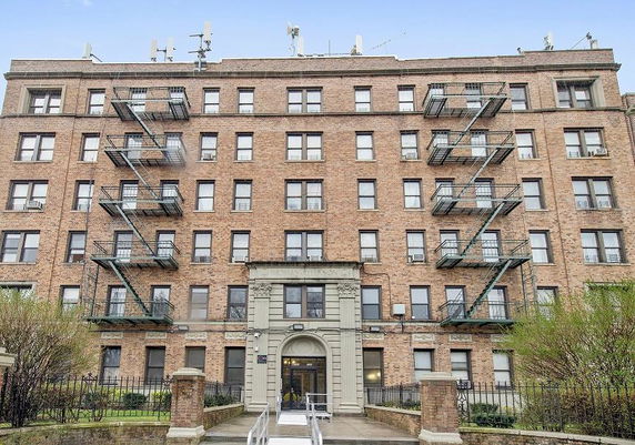 Front view of a multi-story brick apartment building with fire escapes.