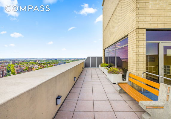 Rooftop area with seating and planters on a tall building, offering a view of the city below.