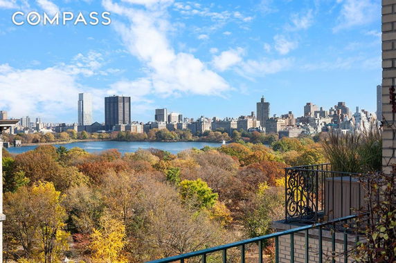 Panoramic view of a city skyline with trees and a body of water in the foreground.