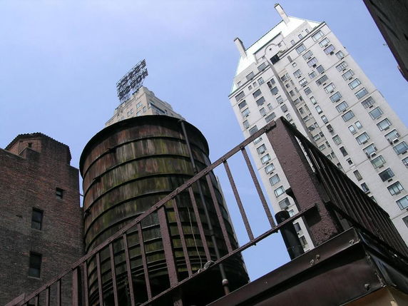 Rooftop view with a large water tank and tall buildings in the background.