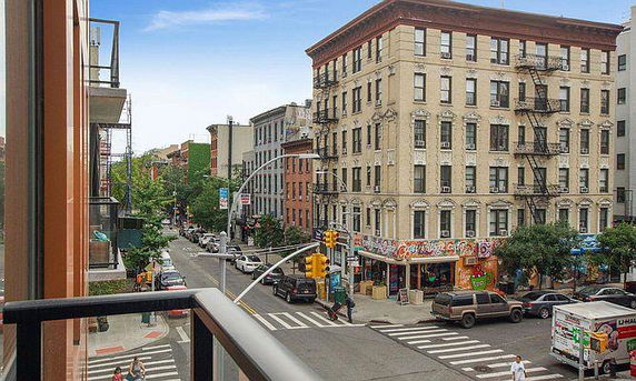 View of a city street with buildings and shops from a balcony perspective.