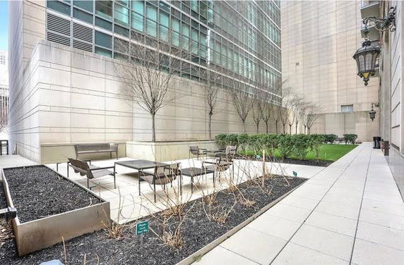 Outdoor seating area next to modern building with trees and planters.